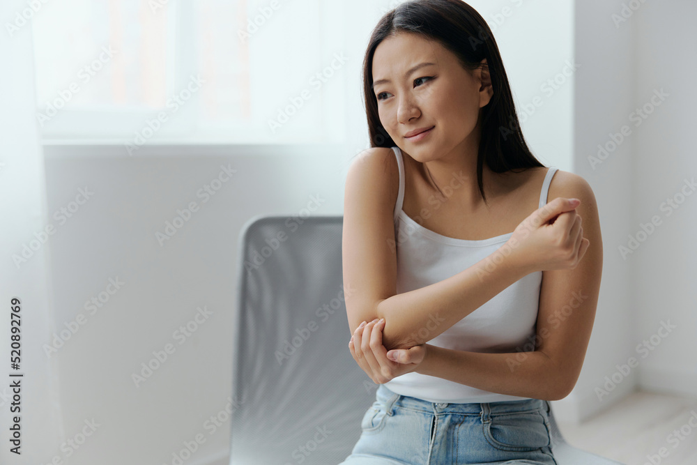Tormented suffering tanned beautiful young Asian woman hurting holding painful elbow at home interior living room. Injuries Poor health Illness concept. Cool offer Banner