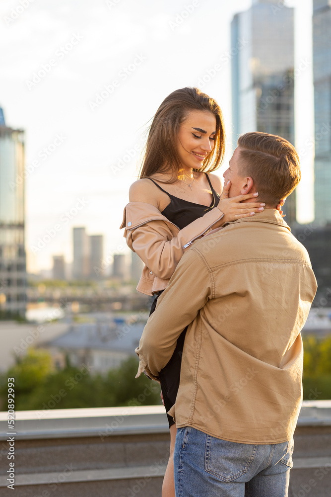Beautiful happy young loving couple on a surprise date on a Saint Valentine's Day. Romantic date on the rooftop, summertime. Young man and beautiful girl. Newlyweds on honeymoon. Golden hour
