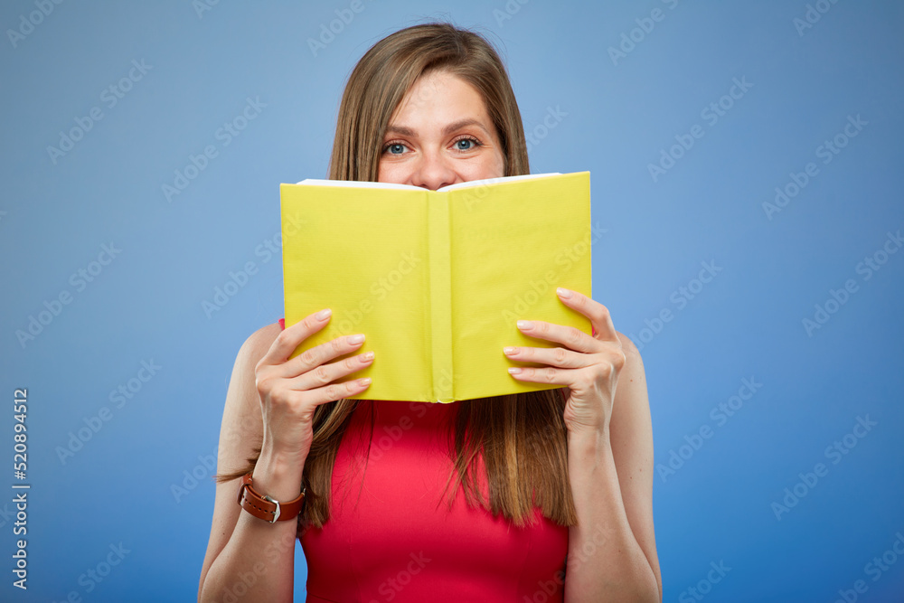 Student lady in red dress holding yellow book in front of face, isolated portrait on blue background. Student lady in red dress holding yellow book in front of face, isolated portrait on blue background.
