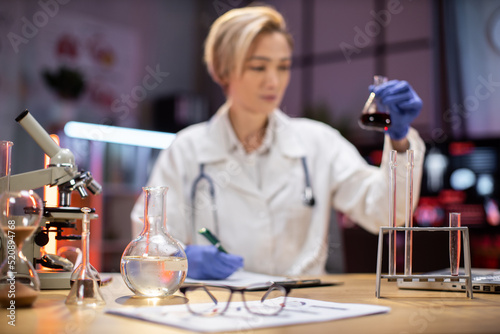 Focus on test tube. Scientific innovations. Positive smart enthusiastic woman scientist looking at the test tubes and smiling while developing a vaccine.