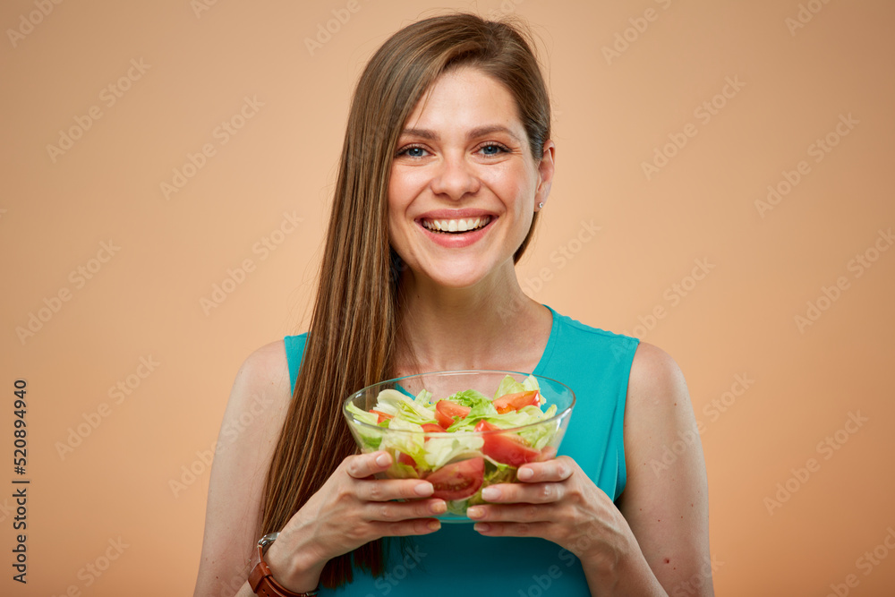 Young lady in azure dress holding green salad in glass bowl, isolated portrait on peach color background Young lady in azure dress holding green salad in glass bowl, isolated portrait on peach color background