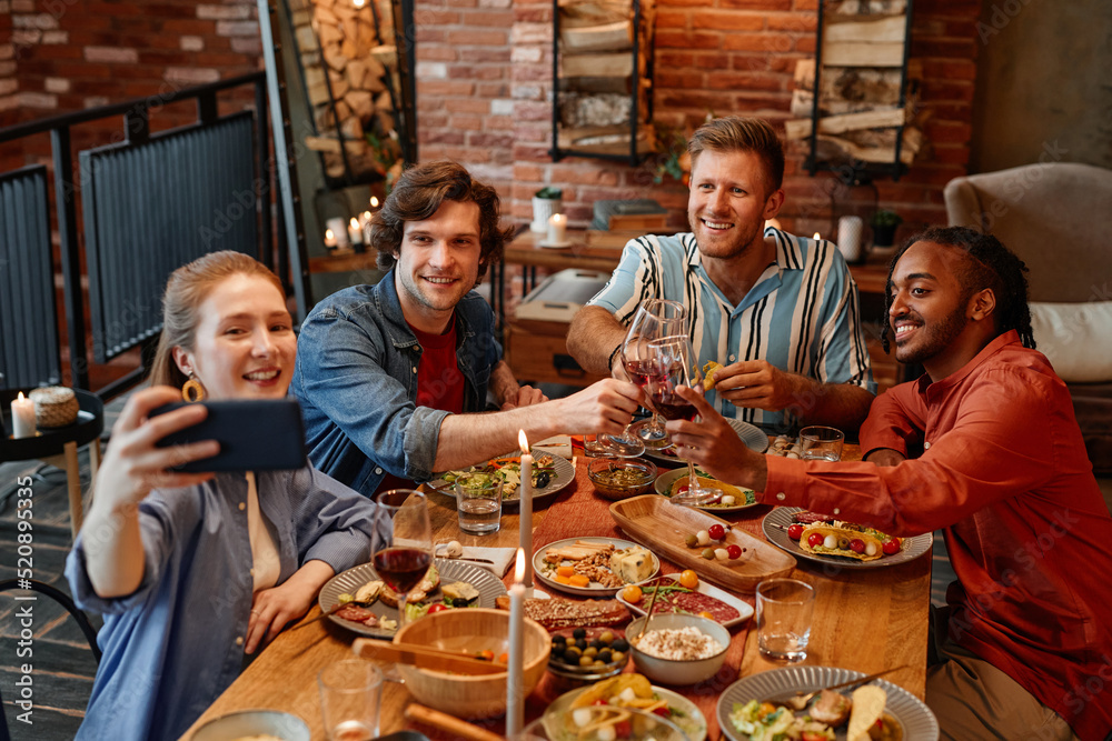 High angle view at group of friends taking selfie photo at table during dinner party and clinking glasses