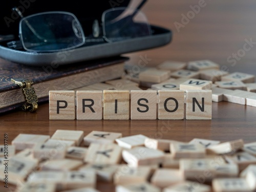 prison word or concept represented by wooden letter tiles on a wooden table with glasses and a book