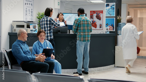 Busy hospital reception desk with diverse people in waiting room  asian and african american man using reports to attend medical appointment. Waiting room lobby at facility clinic.
