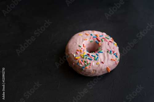 detalle de pan de dona o rosquilla glaseada con chispas de colores y fresa sobre fondo negro con textura photo