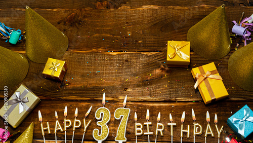 golden letters of the candle with the number happy birthday, the background of the gift boxes with candles happy birthday on the background of brown boards. Copy spacePostcard Happy birthday 37. photo