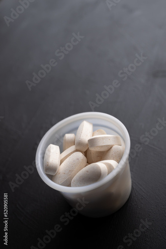 bote de plástico lleno de comprimidos o pastillas de calcio y colágeno hidrolizado sobre fondo negro 