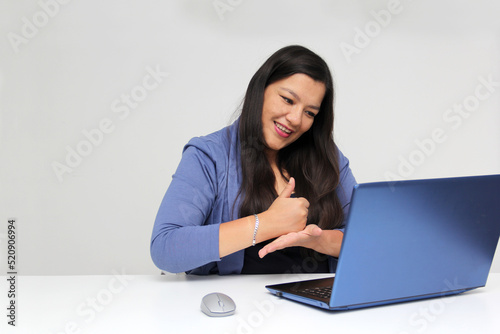 Latino adult woman speaks Mexican sign language with a deaf person through a laptop in a video call

