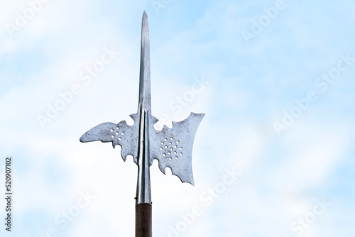 Metal top of a halberd, also called halbard, halbert or Swiss voulge, with axe blade and spike against a cloudy blue sky, pole weapon, copy space