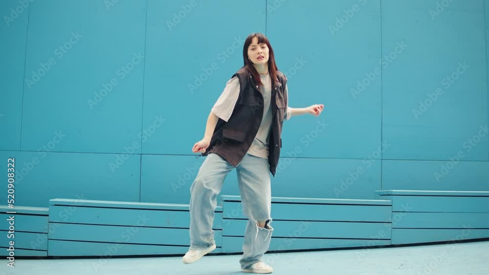 Young woman dancing hip hop on blue background wall. Modern dance choreography. Female professional street dancer showing dance movings. Musical video.