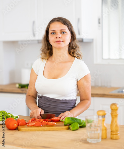 Portrait of woman standing at table in kitchen and cooking salad.