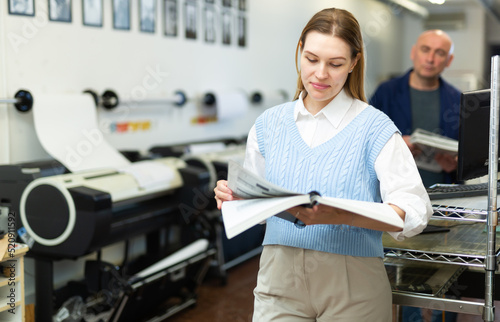 Female publishing facility manager reading operation manual for large printer.
