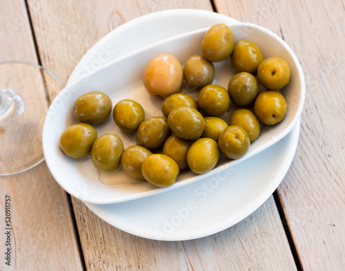 Closeup of plate of pickled green olives with a stone, spanish appetizer