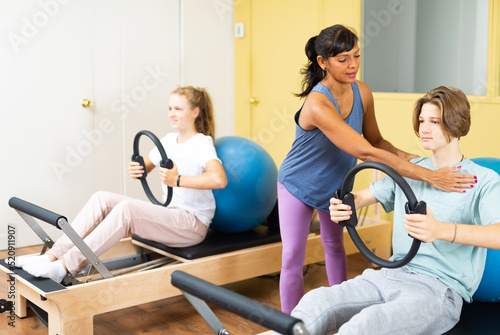 Teenager boy and girl exercising with pilates trainer latin woman in gym. They're training with pilates rings and fitness balls.