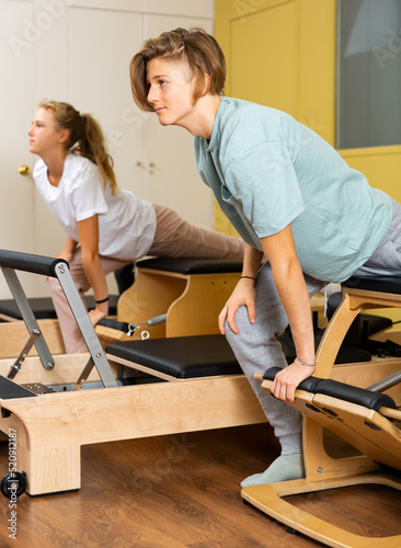 Teen boy and girl in sportswear keeps the balance, pilates training on exercise machine in gym. Fitness workuot in sport club photo