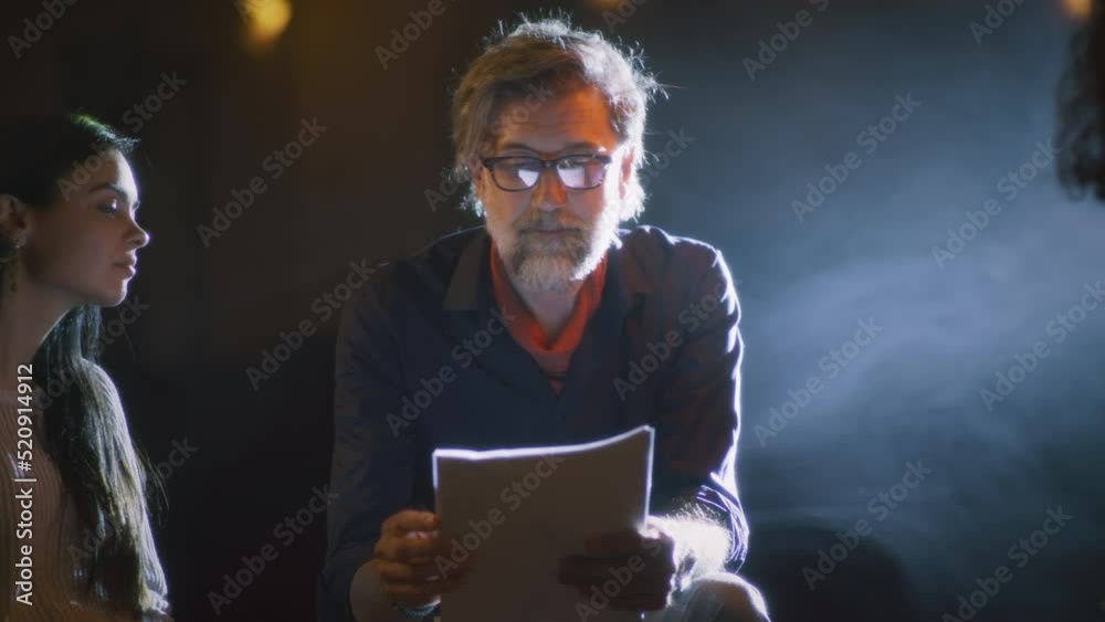 Theater director discussing with the actors the script of the future performance while sitting on a dim stage illuminated by a spotlight