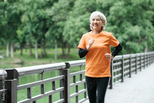 Athletic Senior woman running outdoor jogging in park. Happy retriment age photo