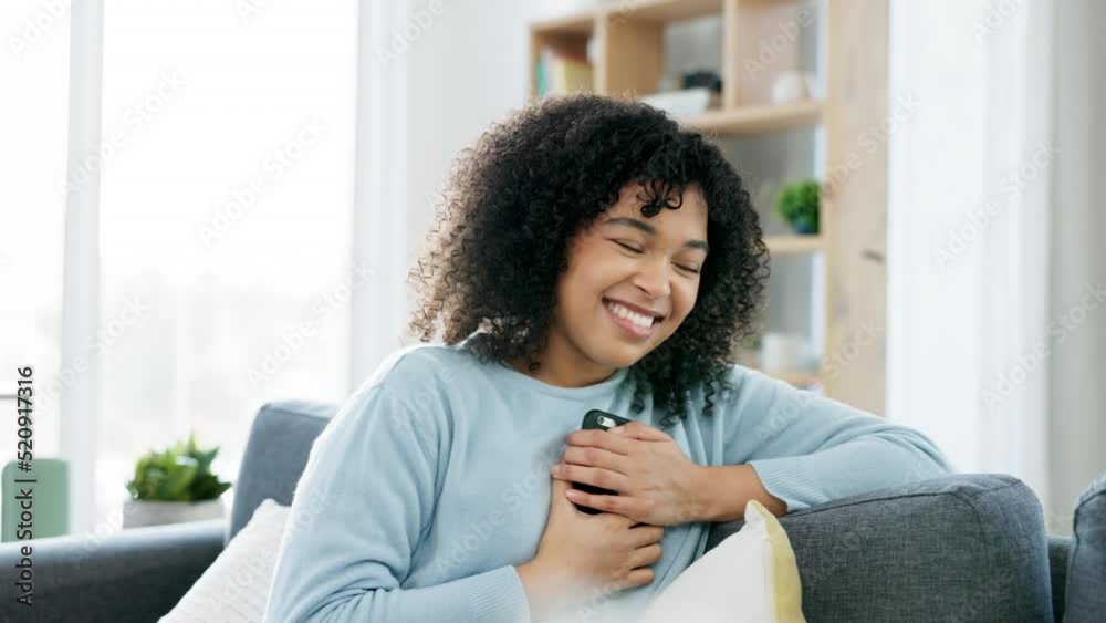 Woman smiling holding a phone and reading a loving text message, email or social media post while sitting on the couch at home. One happy, excited and smiling black female looking browsing the web Woman smiling holding a phone and reading a loving text message, email or social media post while sitting on the couch at home. One happy, excited and smiling black female looking browsing the web