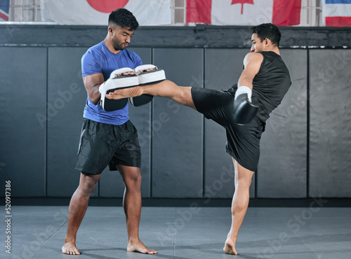 Active, athletes and fit men kick boxing and doing sport training workout in a gym. Two male partners or MMA boxer and trainer practice sparring exercises for a healthy wellness lifestyle. photo