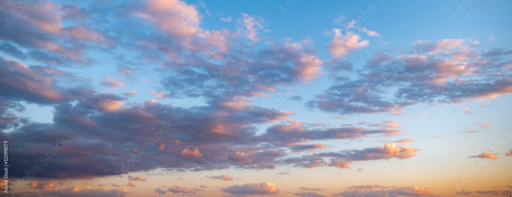Evening blue sky and gray clouds with orange and pink highlights reflecting setting or rising sun, at dusk or dawn.