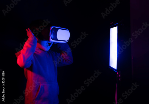 little boy in front of a white screen light playing with virtual reality glasses in a futuristic environment of neon colors. High quality photo