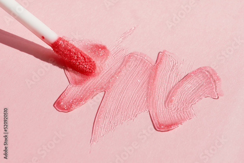 Smears of shining lip gloss and lip gloss brush on pink background, hard shadows photo