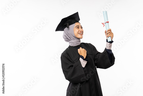 Excited female bachelor graduate wearing a toga excitedly while holding a certificate standing on isolated background photo