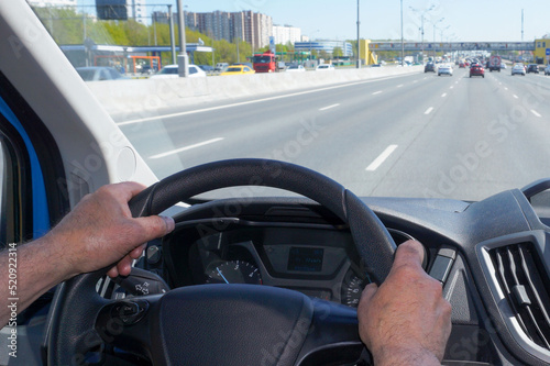  Male hands hold the steering wheel of a car while driving on a highway.