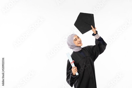 Young graduate Muslim female student in toga holding up black board hat standing on white background photo