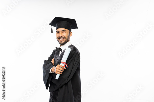 Bearded adult man wearing toga smiling holding certificate paper graduation symbol on white background photo