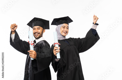 Two confident graduates wearing togas holding certificate while celebrating on isolated background