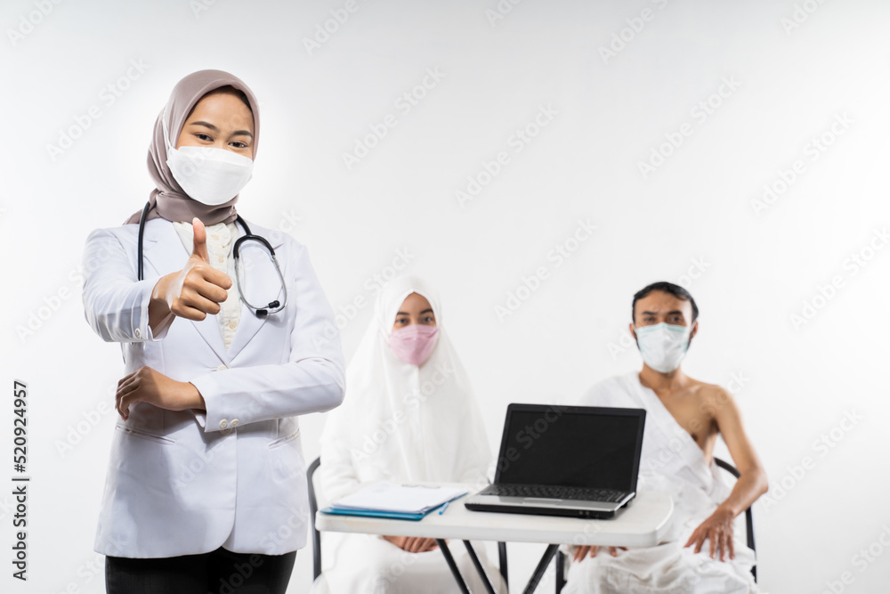 Veiled asian doctor in mask with thumbs up while standing against the background of prospective pilgrims Veiled asian doctor in mask with thumbs up while standing against the background of prospective pilgrims