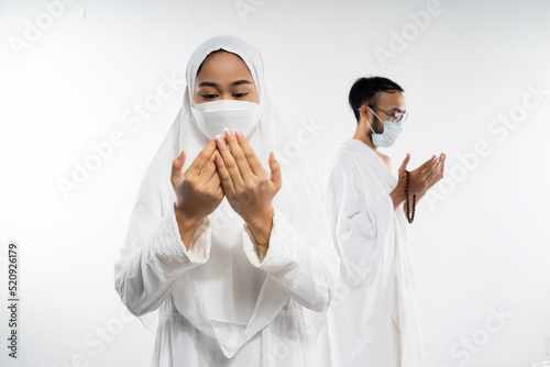 Woman wearing ihram clothes and mask performing al fatihah prayer on isolated background photo