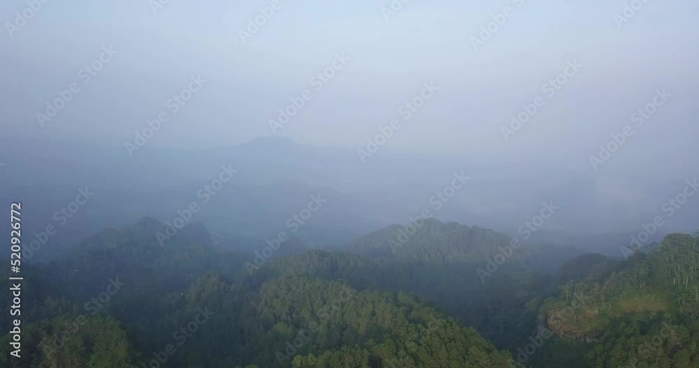 Reveal drone shot over forest overgrown mountains during misty morning in Indonesia. Straight - forward drone flight Reveal drone shot over forest overgrown mountains during misty morning in Indonesia. Straight - forward drone flight