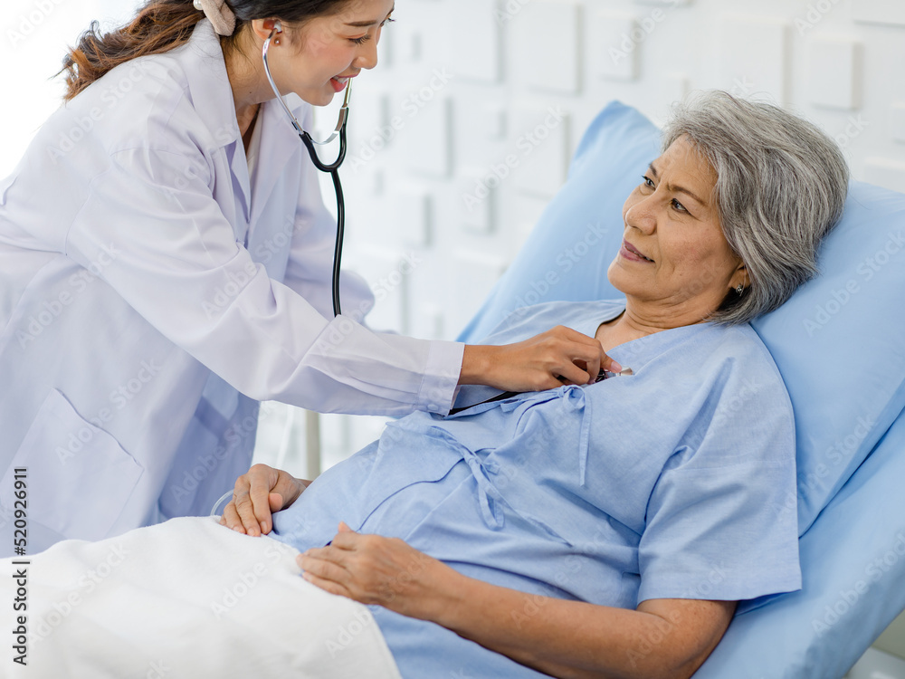 Closeup shot of unrecognizable unknown doctor in white lab coat with stethoscope hand holding comforting supporting old senior unhealthy patient in hospital uniform laying down on bed in ward room Closeup shot of unrecognizable unknown doctor in white lab coat with stethoscope hand holding comforting supporting old senior unhealthy patient in hospital uniform laying down on bed in ward room
