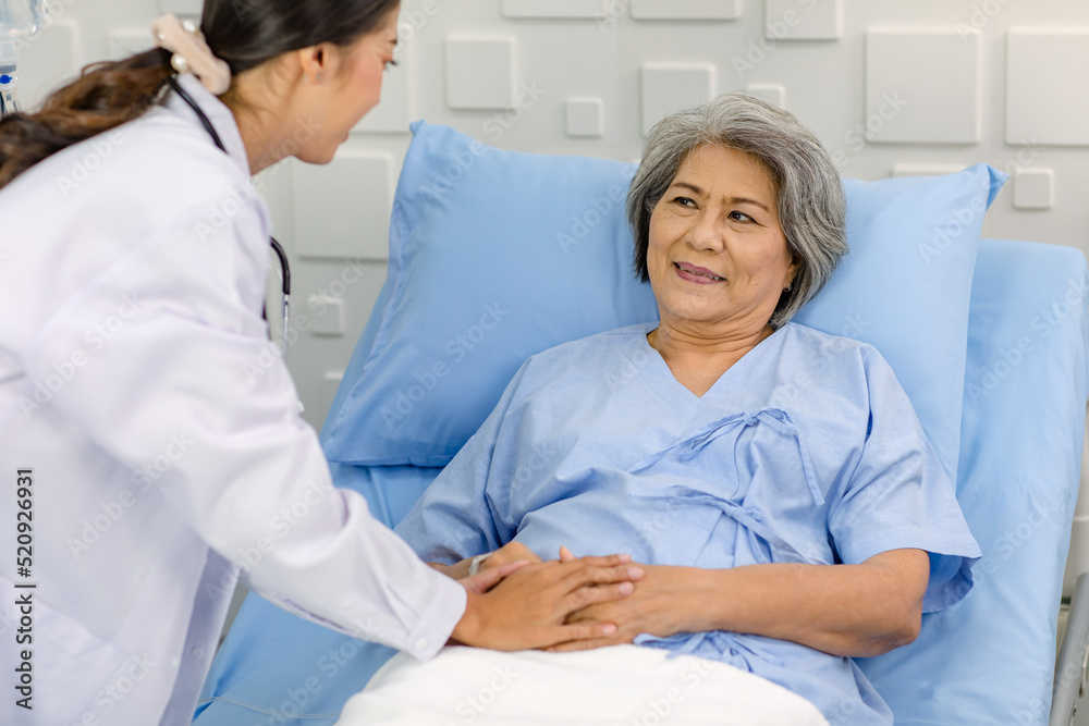 Closeup shot of unrecognizable unknown doctor in white lab coat with stethoscope hand holding comforting supporting old senior unhealthy patient in hospital uniform laying down on bed in ward room Closeup shot of unrecognizable unknown doctor in white lab coat with stethoscope hand holding comforting supporting old senior unhealthy patient in hospital uniform laying down on bed in ward room