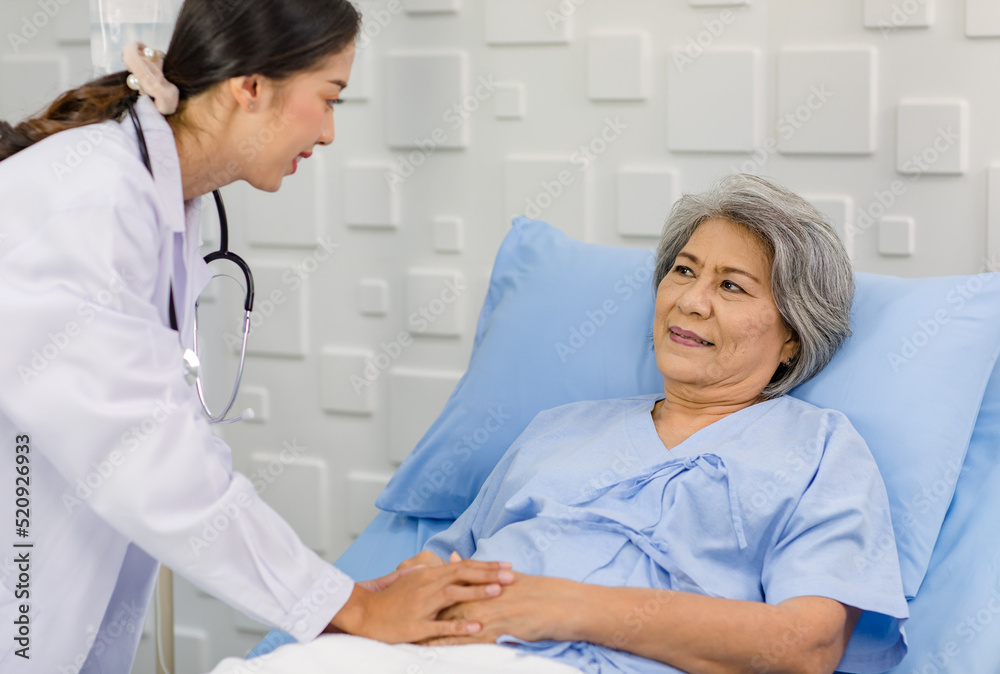 Obraz premium Closeup shot of unrecognizable unknown doctor in white lab coat with stethoscope hand holding comforting supporting old senior unhealthy patient in hospital uniform laying down on bed in ward room