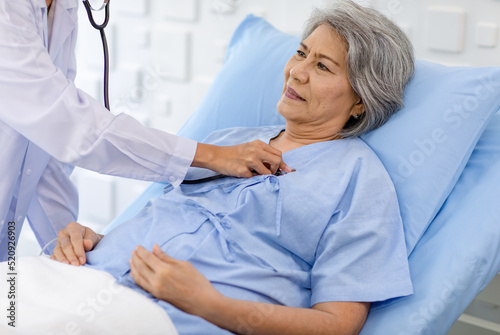 Closeup shot of unrecognizable unknown doctor in white lab coat with stethoscope hand holding comforting supporting old senior unhealthy patient in hospital uniform laying down on bed in ward room