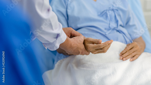 Closeup shot hands of unrecognizable unknown doctor practitioner in white lab coat holding checking examining heartbeat pulse from patient in blue hospital uniform laying down on bed in ward room