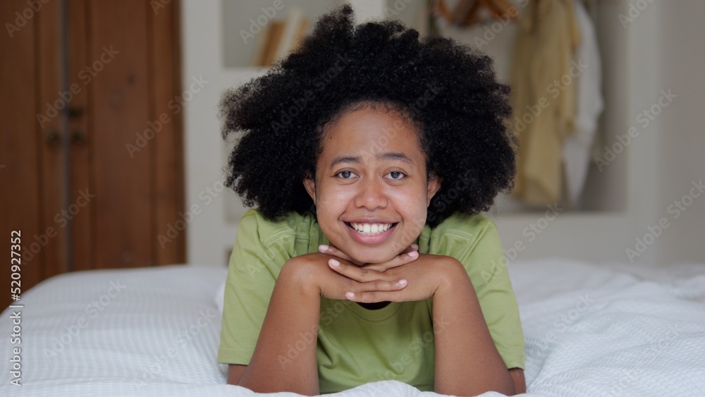 A beautiful black woman with an afro hairstyle lies on the bed and smiles with a snow-white smile and sings songs. Portrait of an Afro Asian woman in a home interior. The life of a multiracial woman. A beautiful black woman with an afro hairstyle lies on the bed and smiles with a snow-white smile and sings songs. Portrait of an Afro Asian woman in a home interior. The life of a multiracial woman.