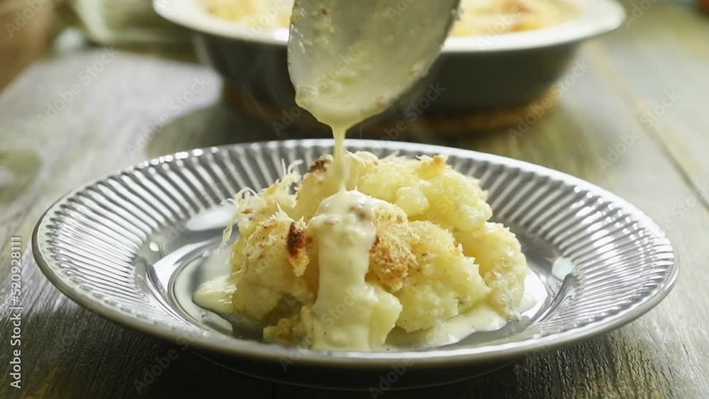 Pouring cheese sauce over the cauliflower gratin.
