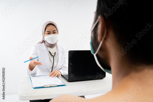 Doctor in a hijab asks a male prospective hajj pilgrim during a health consultation in the room