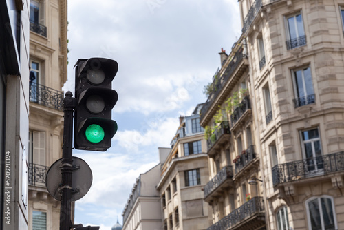 Traffic light with green light with facades of Parisian buildings on a bright day