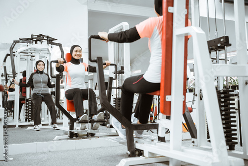 beautiful muslim asian woman using chest press machine during fitness at the gym with friend