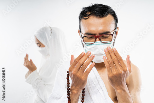 Man wearing ihram clothes and mask performing al fatihah prayer on isolated background photo