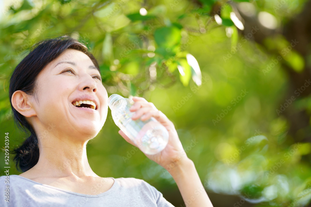 緑の中でペットボトルの水を飲む中年女性