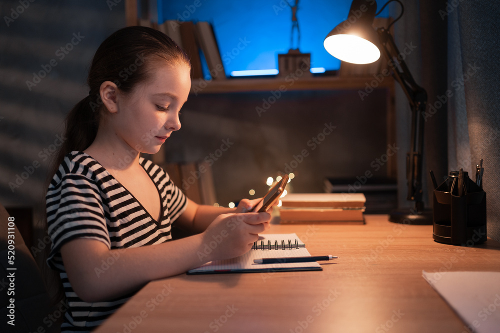 Positive teen girl using doing homework sitting at desk using tablet pad computer, enjoying distance homeschooling at night. Children and education Positive teen girl using doing homework sitting at desk using tablet pad computer, enjoying distance homeschooling at night. Children and education