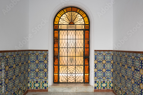 Street view of a beautiful patio entrance in Vejer de la Frontera, Spain. Spectacular wrought iron and colorful glass door surrounded by Azulejos.  photo