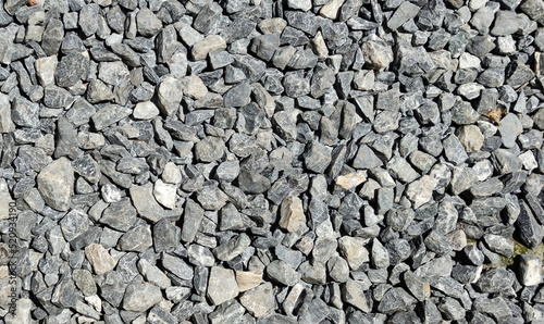 Grey pebbles on the floor against sunlight at noon. Gravel walkway background. The texture of gray gravel on the floor. A random pattern of pebbles.