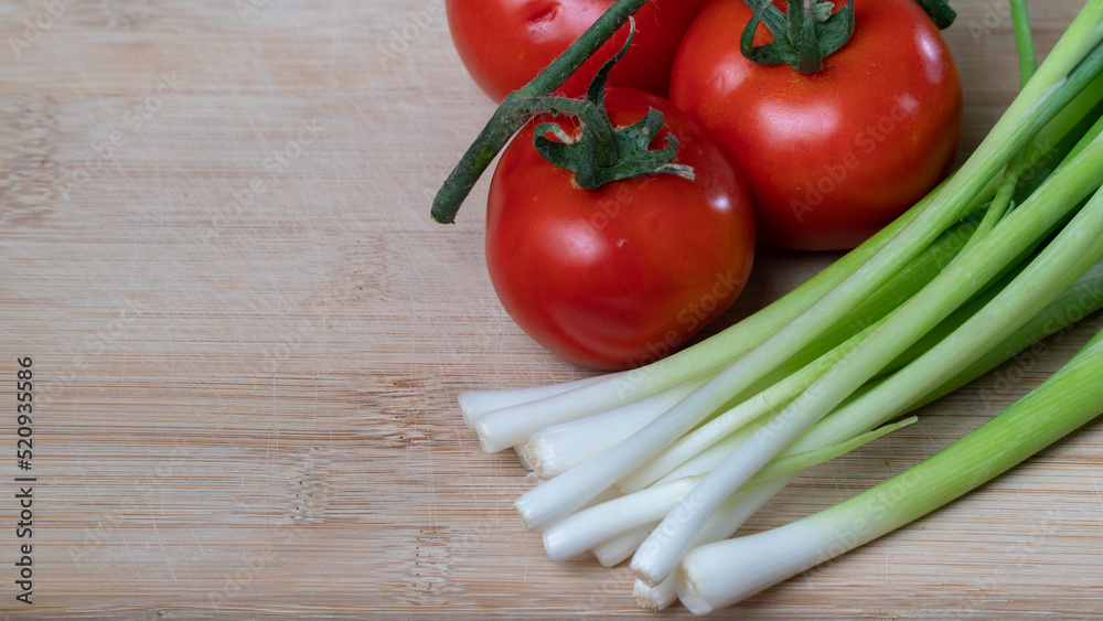 tomatoes on a branch and green onions, vegetables and greens on a wooden background